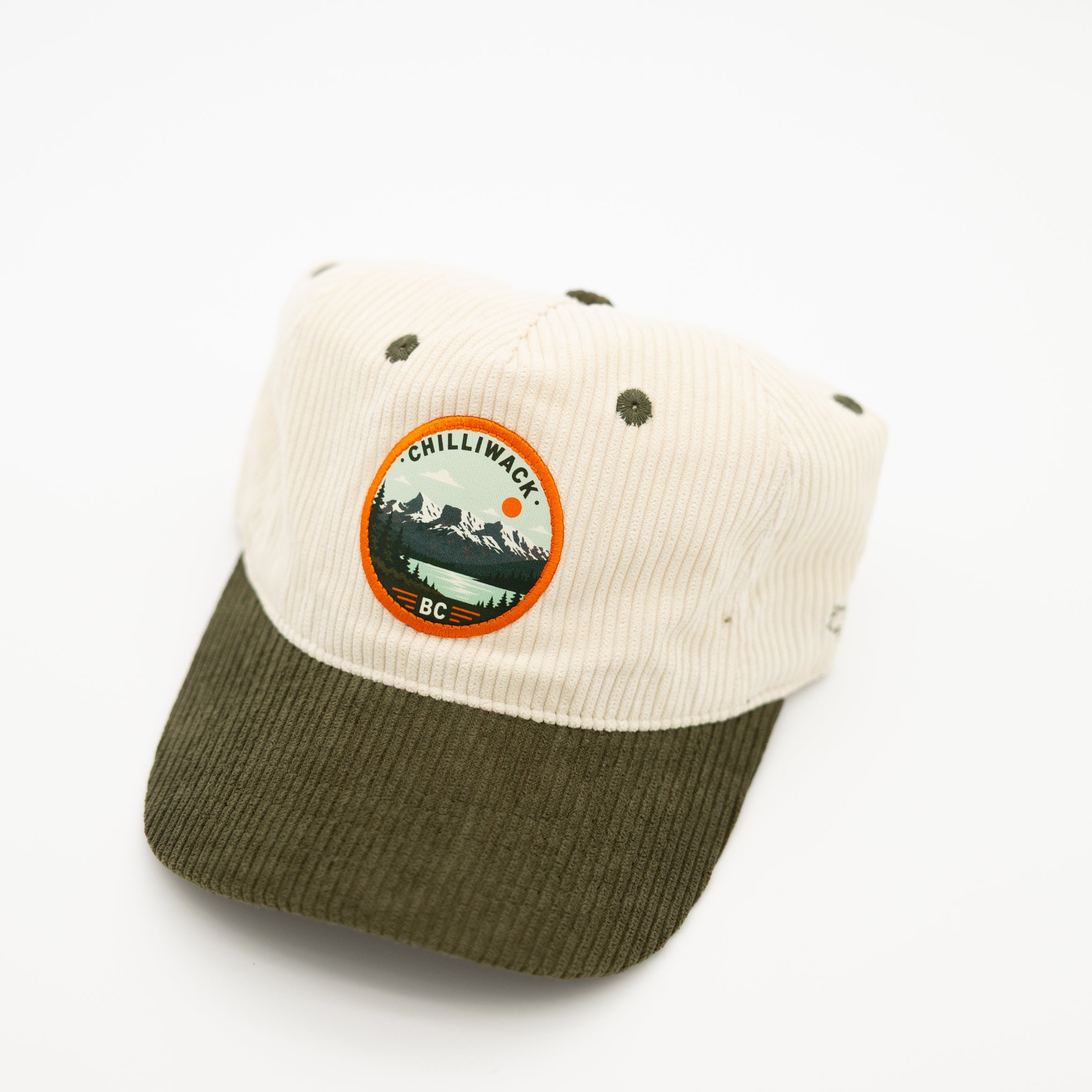 A two-tone corduroy baseball cap with an off-white crown and an olive green brim, featuring a circular 'chilliwack BC' logo patch on the front.