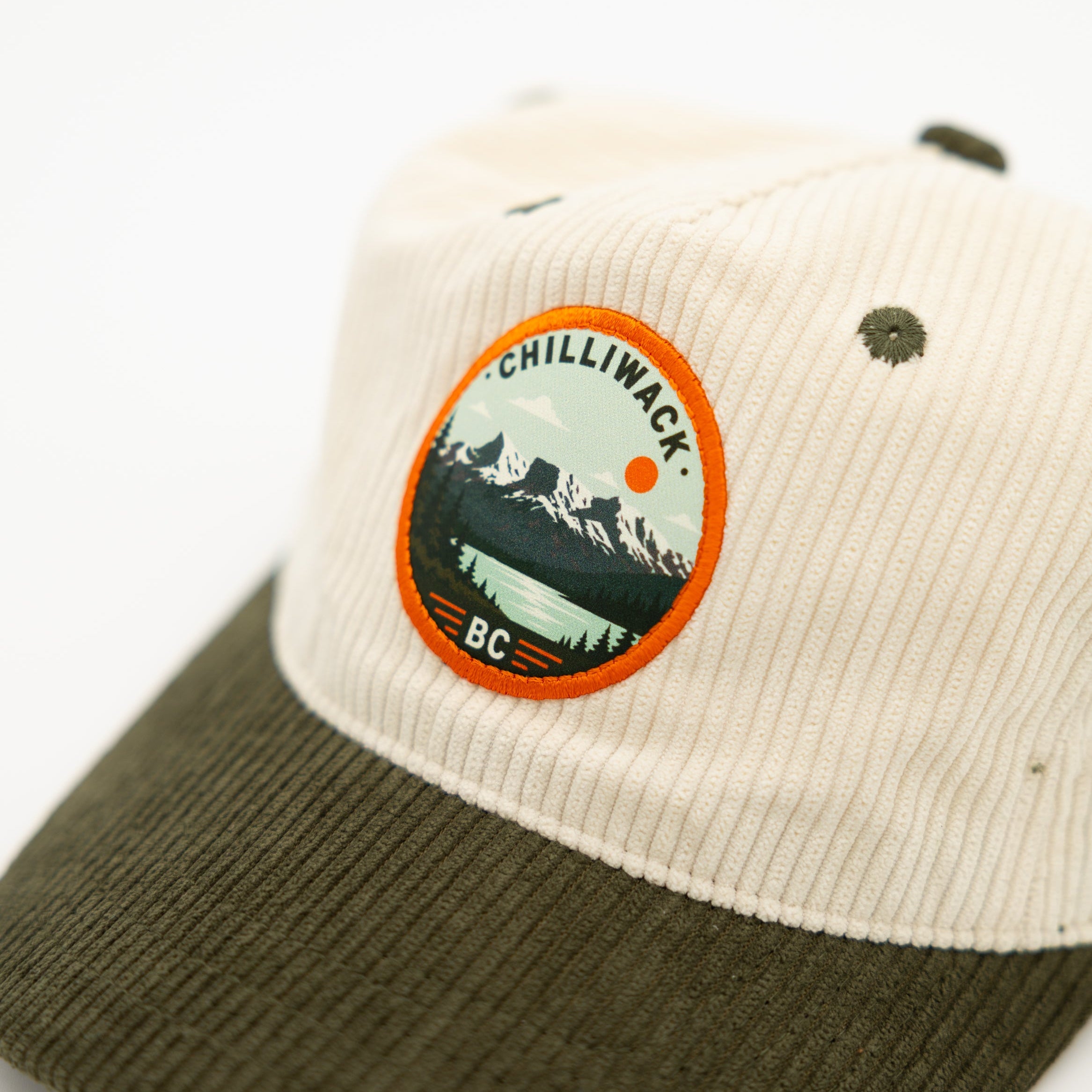 A two-tone corduroy baseball cap with an off-white crown and an olive green brim, featuring a circular 'chilliwack BC' logo patch on the front.