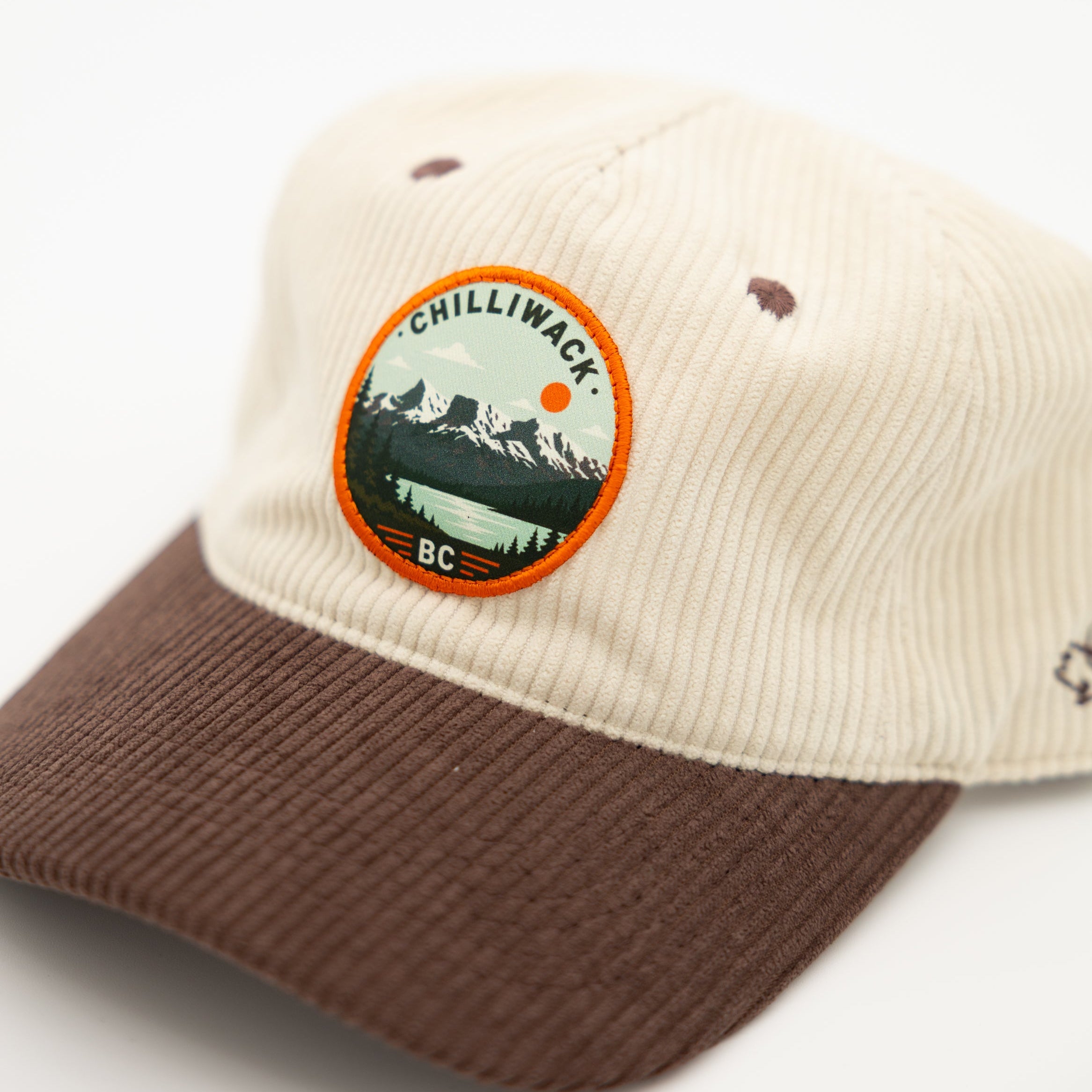 A two-tone corduroy baseball cap with an off-white crown and an brown green brim, featuring a circular 'chilliwack BC' logo patch on the front.