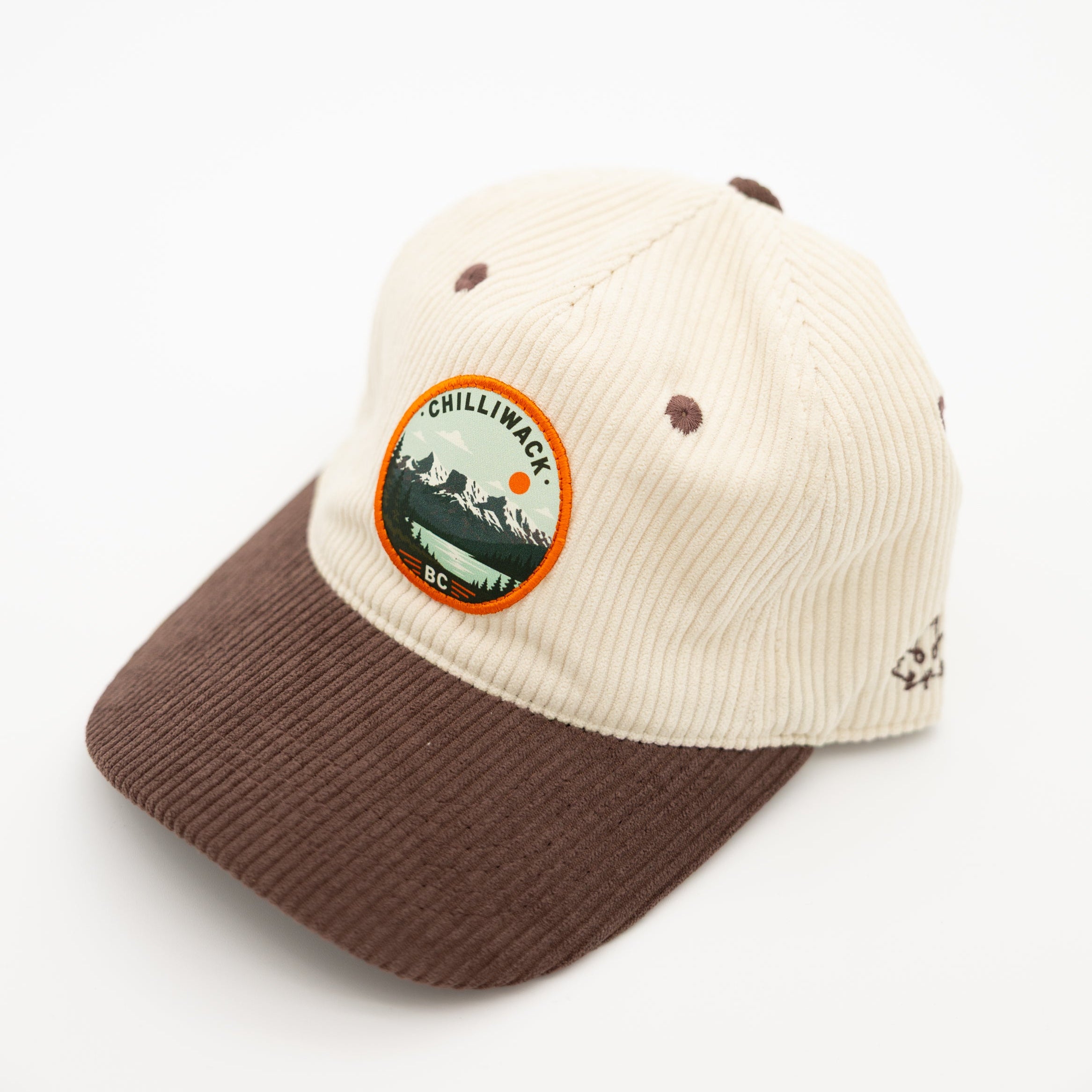 A two-tone corduroy baseball cap with an off-white crown and a brown visor, featuring a circular 'Chilliwack BC' patch on the front and a small embroidered logo on the side.