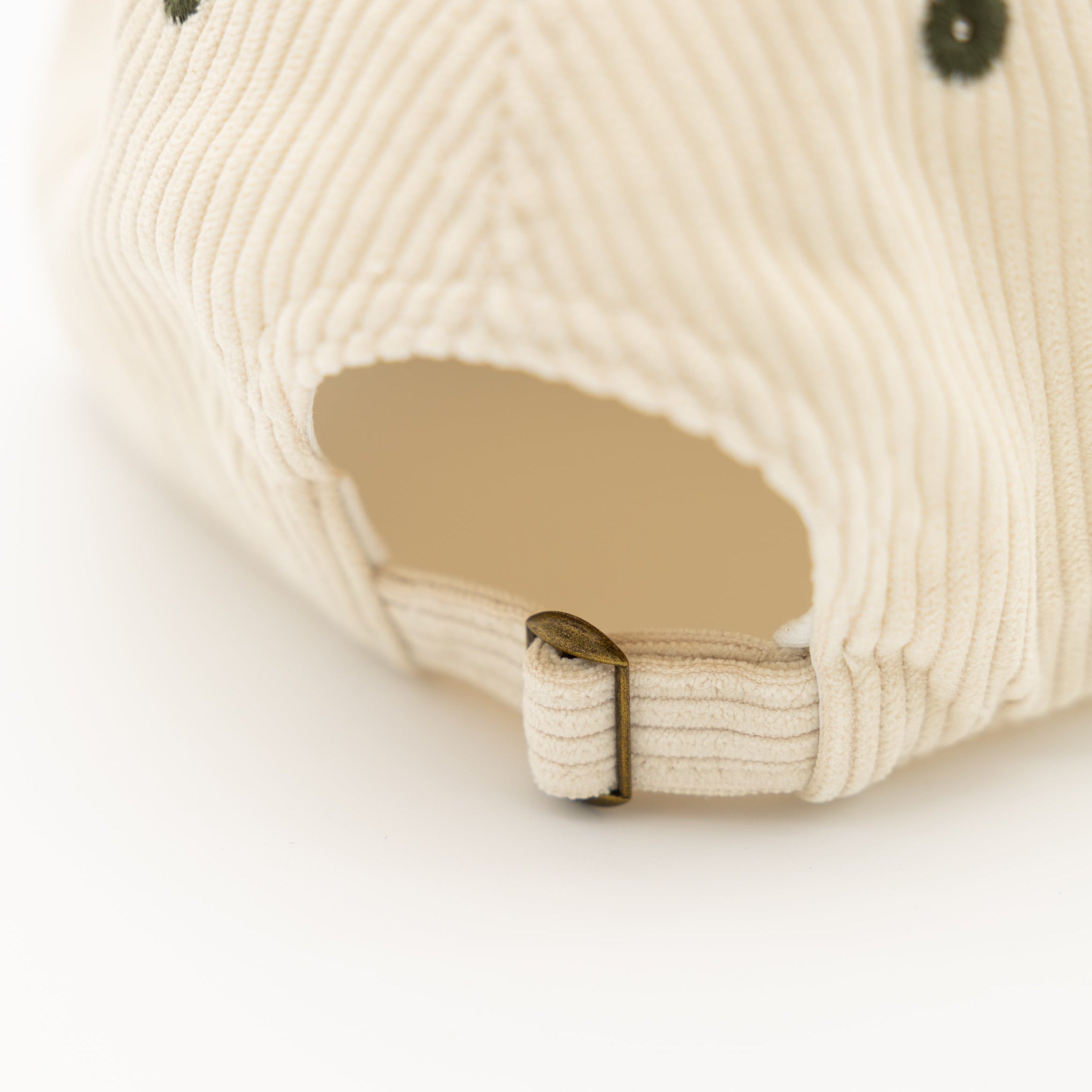 Close-up of the back of a cream-colored ribbed corduroy cap, showing the adjustable fabric strap and metal buckle.