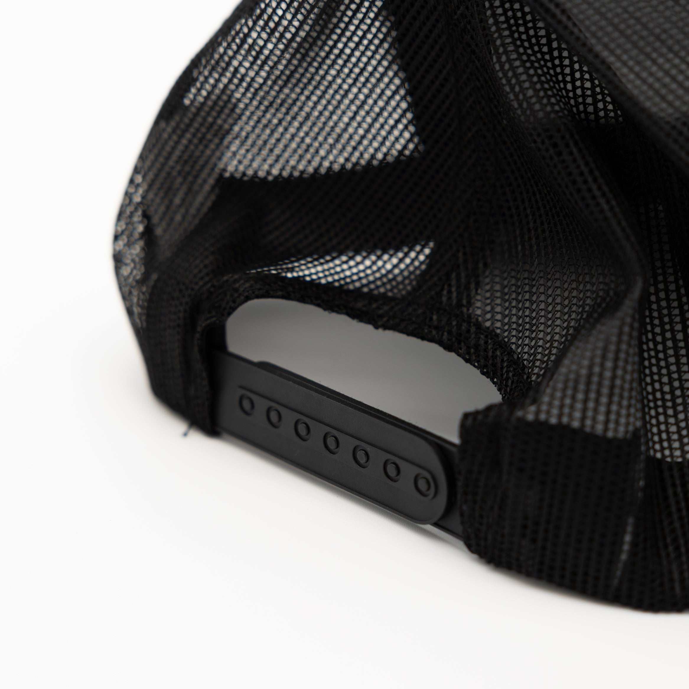 Close-up of the back of a black trucker cap with a black mesh back and a black adjustable snap closure on a white background.