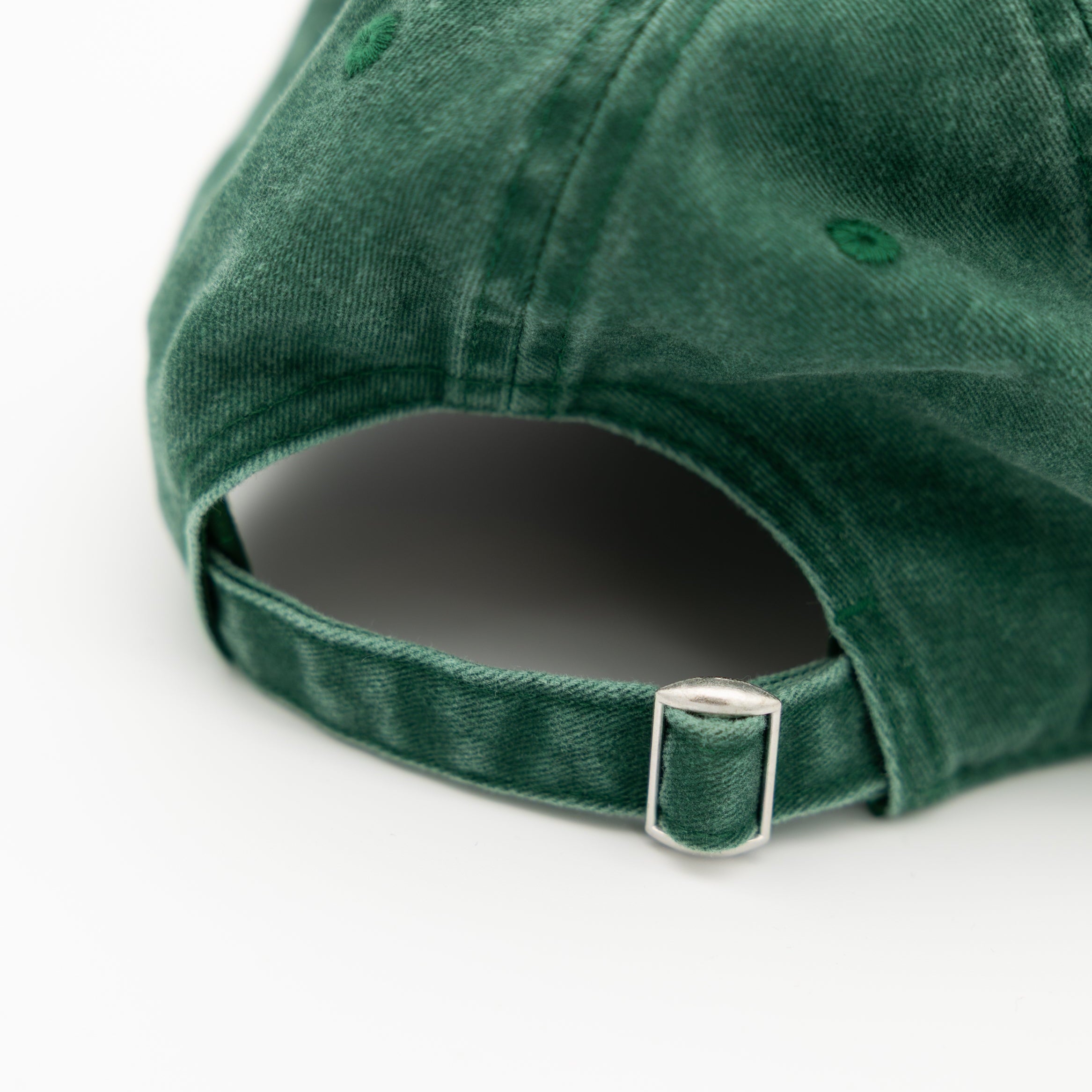 Close-up of the back of a dark green cotton cap with an adjustable strap and silver metal buckle, on a white background.